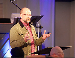 A man speaking at the front of a church to a congregation of men